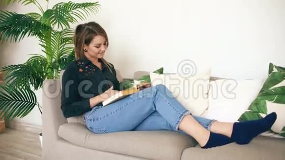 快乐的少女在家看她最喜欢的小说时躺在客厅的沙发上视频的预览图