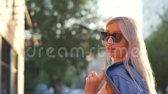 迷人的女孩走在城市的街道上转向相机微笑美丽的金发碧眼视频的预览图