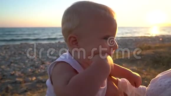 妈妈在日落时分和一个孩子坐在沙滩上视频的预览图