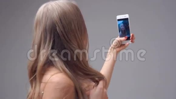 年轻的金发女孩拿着智能手机自拍视频的预览图