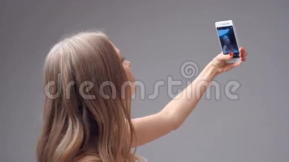 年轻的金发女孩拿着智能手机自拍视频的预览图