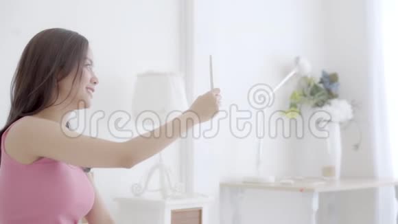 美丽的肖像年轻的亚洲女人坐在卧室里用智能手机自拍早上在家视频的预览图