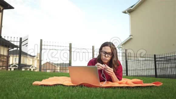 穿着红色衣服的女孩拿着笔记本电脑和耳机躺在后院视频的预览图