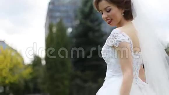 迷人的年轻黑发新娘妆容鲜艳穿着白色连衣裙和面纱在户外靠近视频的预览图