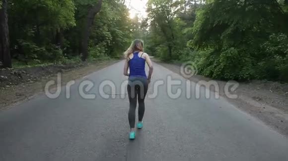 运动的金发女孩在森林的道路上奔跑用安定剂射击视频的预览图