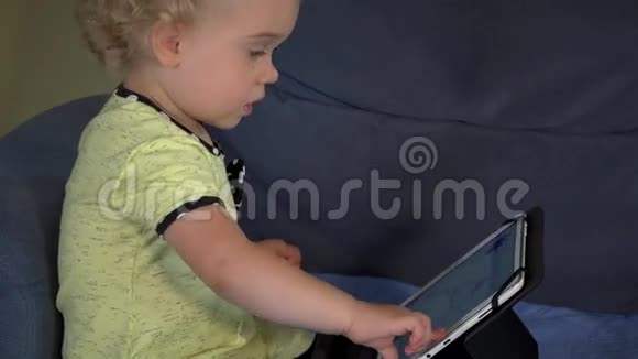 好奇的金发孩子在沙发上摸着平板电脑屏幕视频的预览图