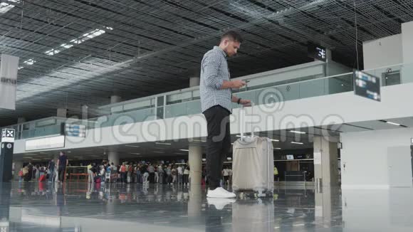 英俊的年轻人使用智能手机在机场工作等待他的排队登记旅行视频的预览图