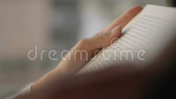 合上雌性的手在看书年轻的女人坐在家里坐在窗户附近看书视频的预览图