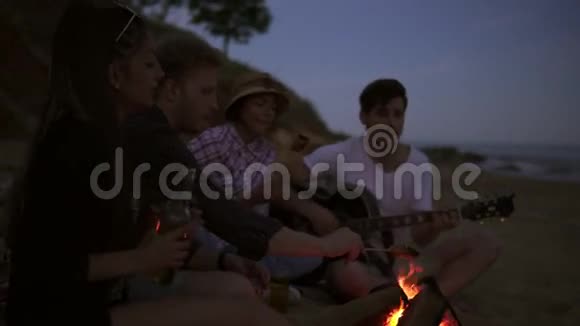 晚上在海滩上用篝火野餐年轻人快乐的朋友唱歌弹吉他视频的预览图