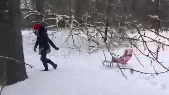 在冬天的树林里妈妈在雪地上拉雪橇手持的4K视频的预览图