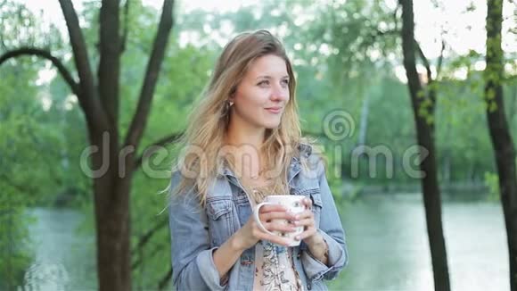留着长发的在模糊的自然背景下手里拿着一杯茶或咖啡是个漂亮女人视频的预览图