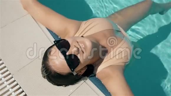 年轻美丽的太阳镜女郎在游泳池享受水视频的预览图
