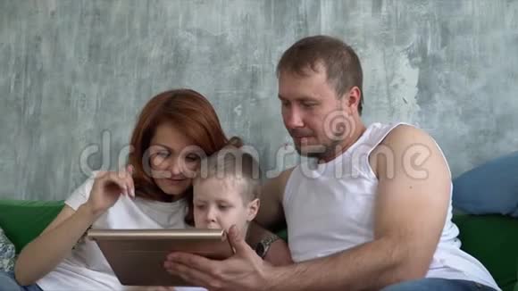 儿子和父母坐在沙发上玩平板电脑有技术的年轻人视频的预览图