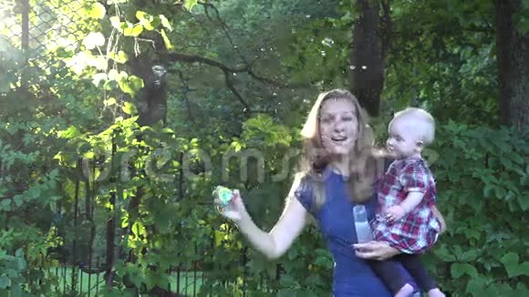 漂亮的金发女人吹肥皂泡漂亮的婴儿在明亮的阳光下享受它4K视频的预览图