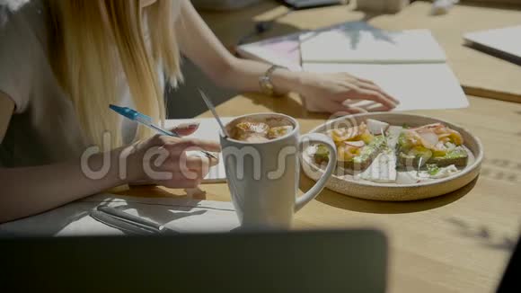 漂亮的女学生在她的电脑上写课程自由职业者女孩通过笔记本电脑在咖啡馆工作写视频的预览图