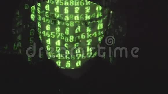在黑暗的办公室里戴着帽子的男性黑客的脸在电脑上工作而绿色的代码字符在他的脸上反射视频的预览图
