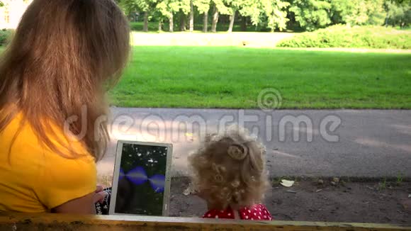 带着小孩的女人在公园长椅上玩平板电脑视频的预览图