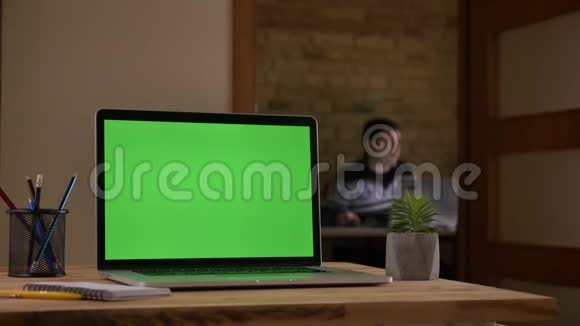 室内办公室的办公桌上放着绿色彩色屏幕的笔记本电脑特写镜头视频的预览图