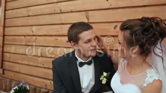 新娘抚摸新郎的脸颊坐在老房子的长凳上视频的预览图