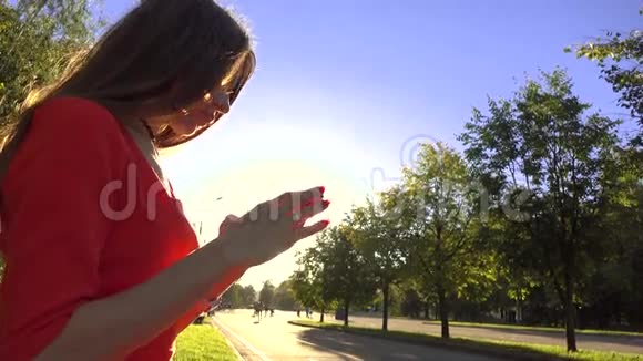美丽的黑发女孩穿着红色连衣裙在公园里用她的智能手机4K视频视频的预览图