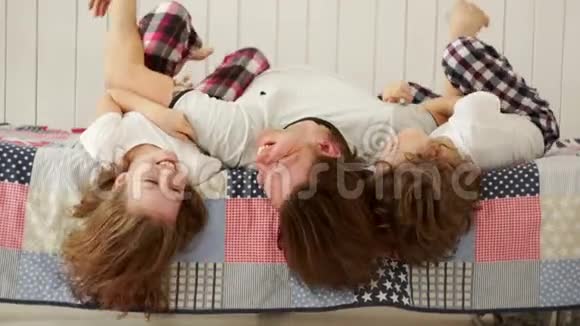 年轻的家庭父亲和他的孩子在床上玩耍视频的预览图