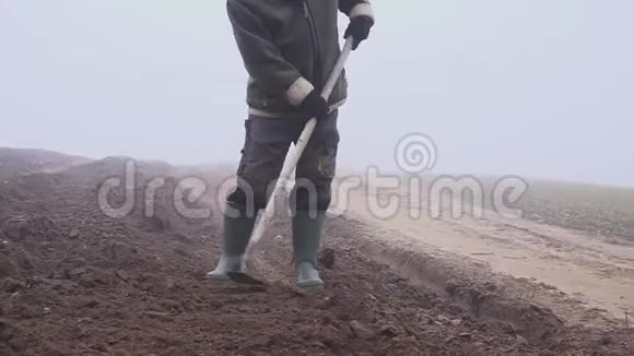 戴着帽子的高级农民手里拿着一把泥泞的锄头和田野上的草叉体力劳动福克视频的预览图