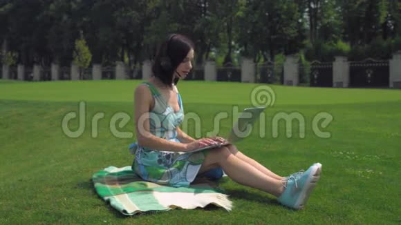 一个年轻女孩坐在毯子上在户外用笔记本电脑打字视频的预览图