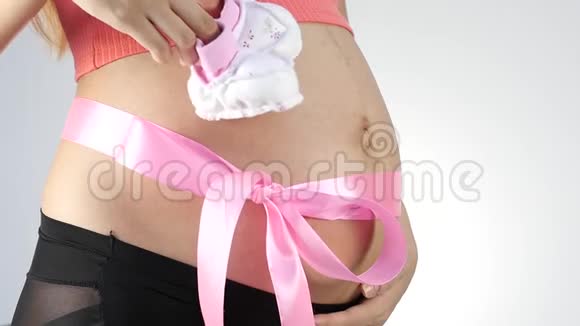 穿着内衣的怀孕妈妈在玩婴儿鞋腹部有粉红色的丝带慢动作视频的预览图