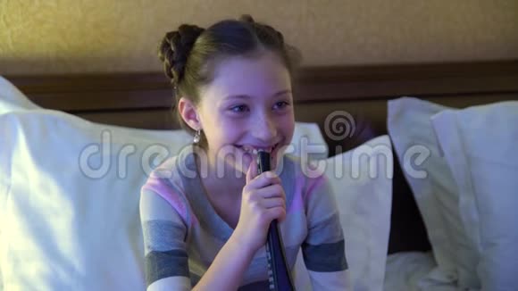 漂亮的小女孩坐在旅馆的床上看电视手里拿着遥控器的女孩视频的预览图