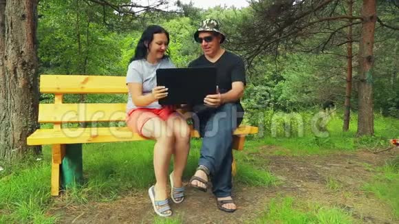一个男人和一个女人在公园的长凳上用笔记本电脑工作视频的预览图