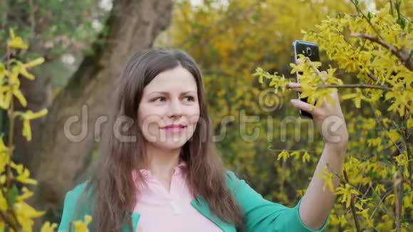 穿绿色夹克的漂亮女孩在黄花树上自拍视频的预览图