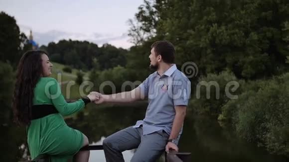 一对夫妇坐在公园的湖边手牵手视频的预览图