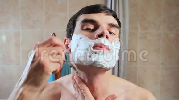 一个人用剃刀在泡沫中剃了他的脸他在镜子前刮胡子视频的预览图
