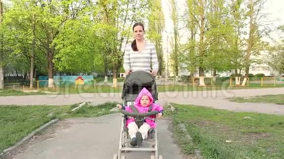 妈妈穿着一个小女孩坐在婴儿车里沿着小路走视频的预览图