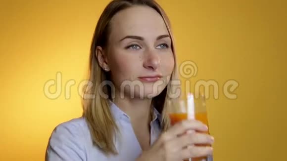 一位漂亮的年轻貌美的女士在黄色背景下从杯子里喝果汁视频的预览图