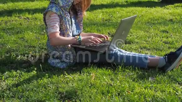 在大自然中做笔记本电脑的青少年那个女孩坐在公园的草地上在一个阳光明媚的日子里带着笔记本电脑在新鲜空气中视频的预览图
