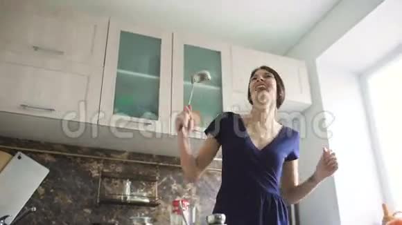 有趣的女人家庭主妇在家里的现代厨房里做饭时用大勺子跳舞唱歌视频的预览图
