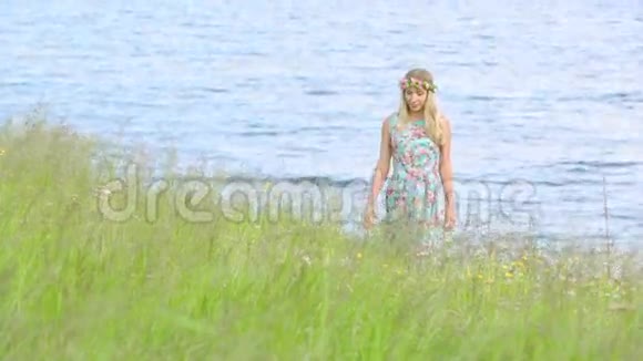 美丽的女孩穿着花圈走在草地上年轻人穿着时尚的带花印的连衣裙视频的预览图