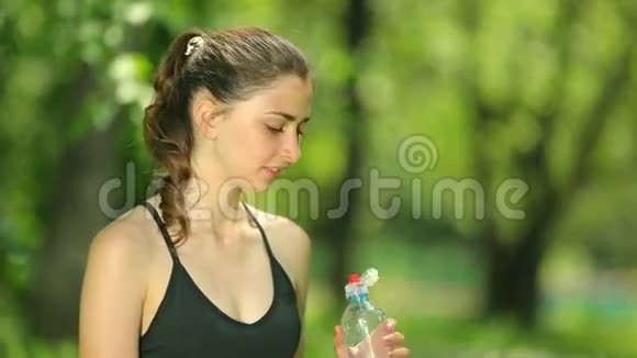 苗条的年轻女人在训练后喝水女运动员休息她喝水在炎热的跑步中外出视频的预览图