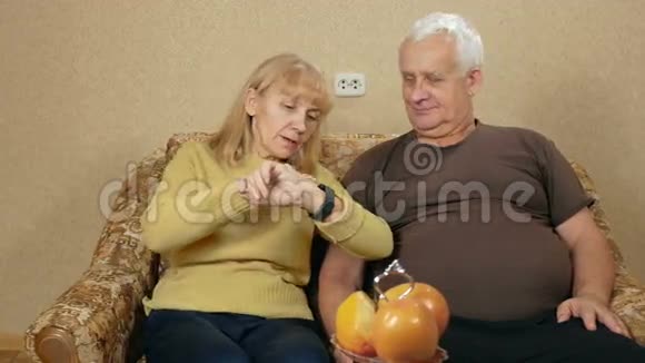 年长夫妇在家里的沙发上看智能手表上的信息他们仔细阅读并阅读重要的文章视频的预览图