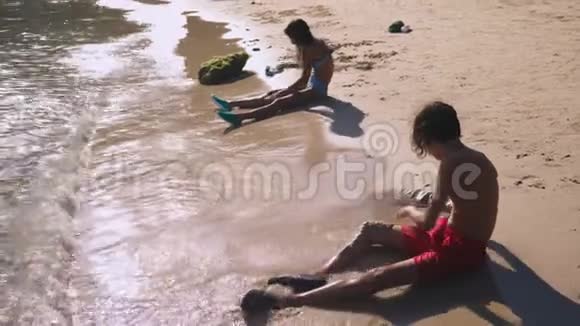 在热带海滩上做沙滩城堡的青少年兄妹视频的预览图