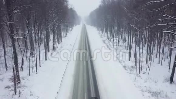 降雪时被冬季森林包围的道路上的交通鸟瞰图视频的预览图