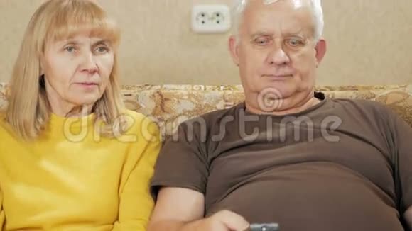一对老夫妇在家里沙发上看电视女人笑着选择电视遥控器本身视频的预览图