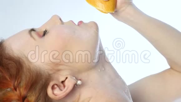 年轻女子把橘子塞进嘴里在你脖子上的白色背景上慢动作视频的预览图