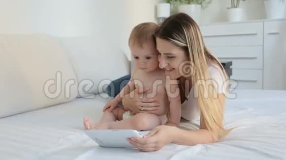 美丽的年轻母亲和她的小儿子在卧室里看数码平板上的卡通片视频的预览图