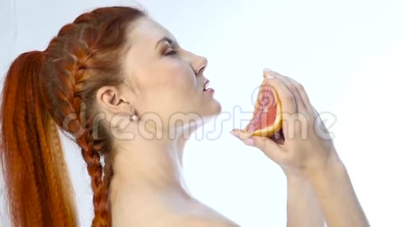 年轻女子把橘子塞进嘴里在你脖子上的白色背景上慢动作视频的预览图