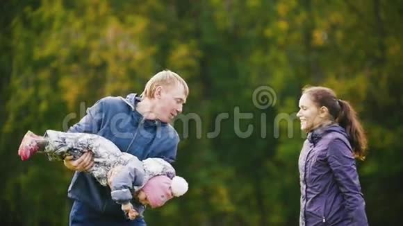 幸福的家庭父亲母亲和孩子在秋天公园散步的小女孩在草地上玩耍动作缓慢视频的预览图