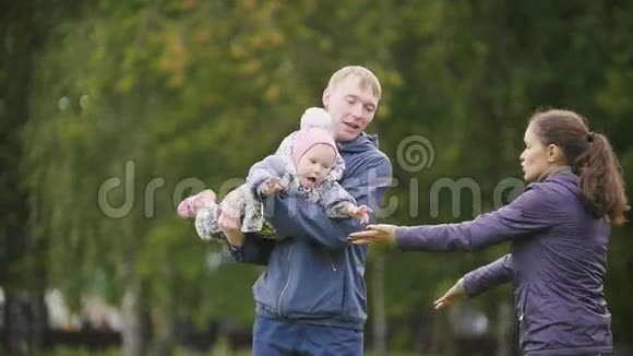幸福的家庭父亲母亲和孩子在秋天公园散步的小女孩一个女人拥抱一个男人和一个孩子慢动作视频的预览图