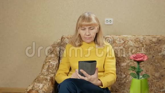 在家休息的女人在沙发上为平板电脑她翻阅着书页仔细阅读假期回家视频的预览图