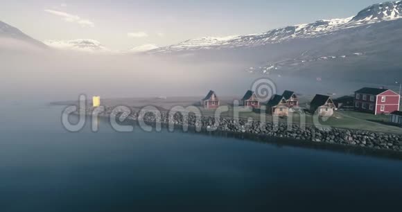 在清晨的阳光下在峡湾和斯堪的纳维亚建筑上空低飞冰岛视频的预览图